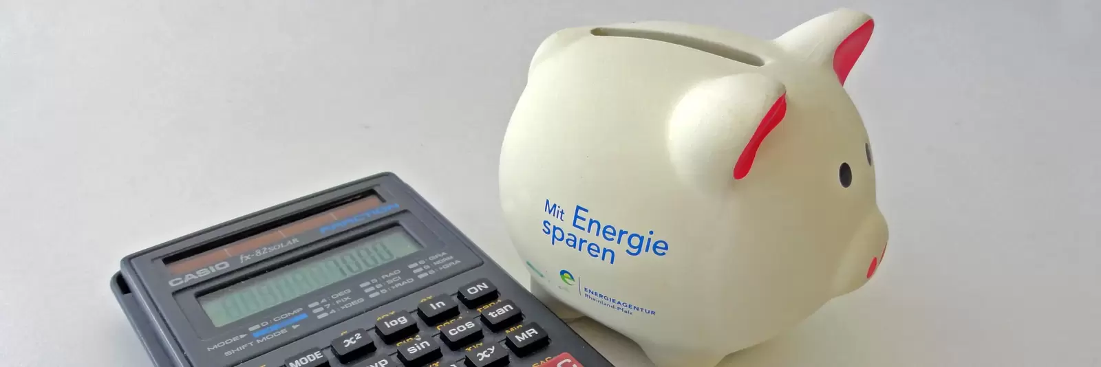 Taschenrechner und Sparschwein mit Aufschrift "Mit Energie sparen"