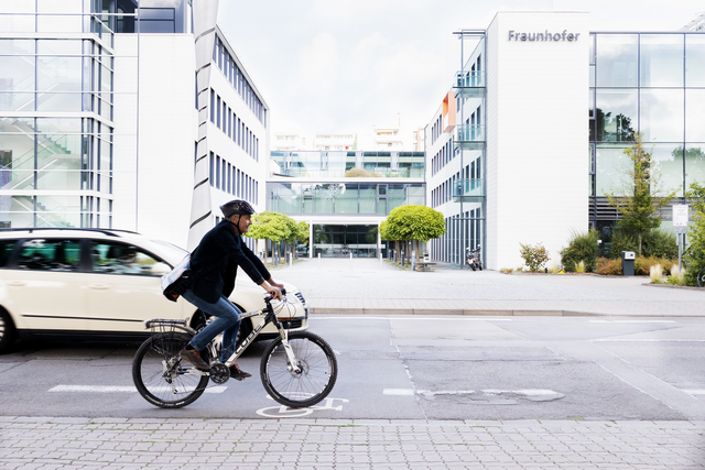 Radfahrer und Auto vor urbanem Hintergrund