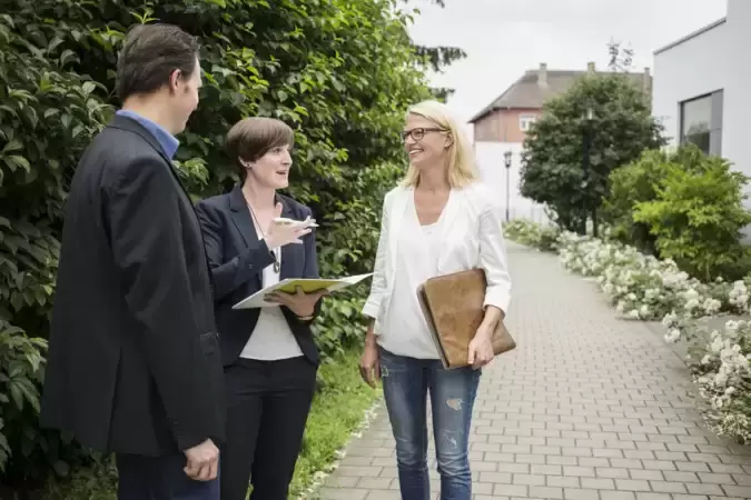 Drei Personen stehen auf einem Weg im Freien und besprechen etwas.