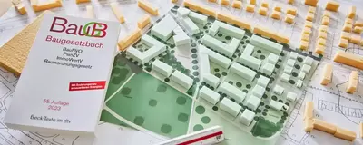 Das Modell einer Stadt liegt auf dem Tisch, daneben das Baugesetzbuch